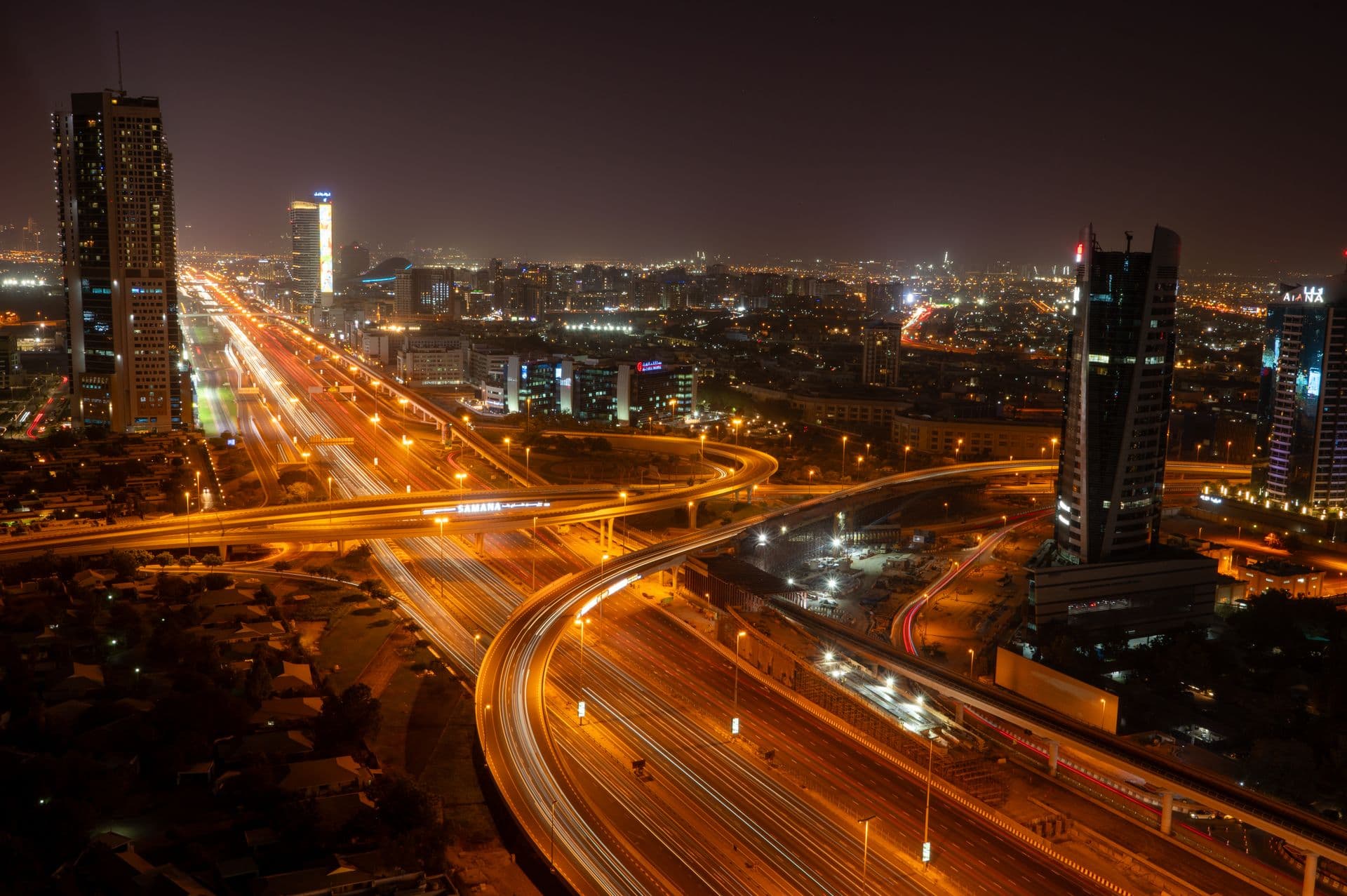 Dubai multi-level road interchange after dark, with long red and white light trails from traffic sweeping across the flyovers